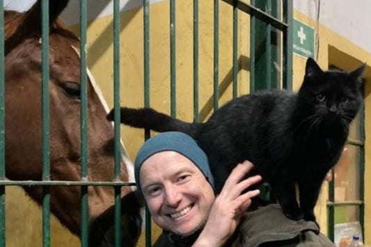 Bild von Tierheilpraktiker Tom Steinmetz mit eine Katze auf der Schulter und einem lieb guckenden Pferd.