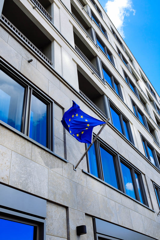 Europäische Union Flagge weht außerhalb eines modernen Bürogebäudes, repräsentiert regulatorische Rahmenbedingungen für den Verkauf und die Verteilung von medizinischen und heilenden Pilzen, oder Vitalpilze und Heilpilze, auf dem EU-Markt.